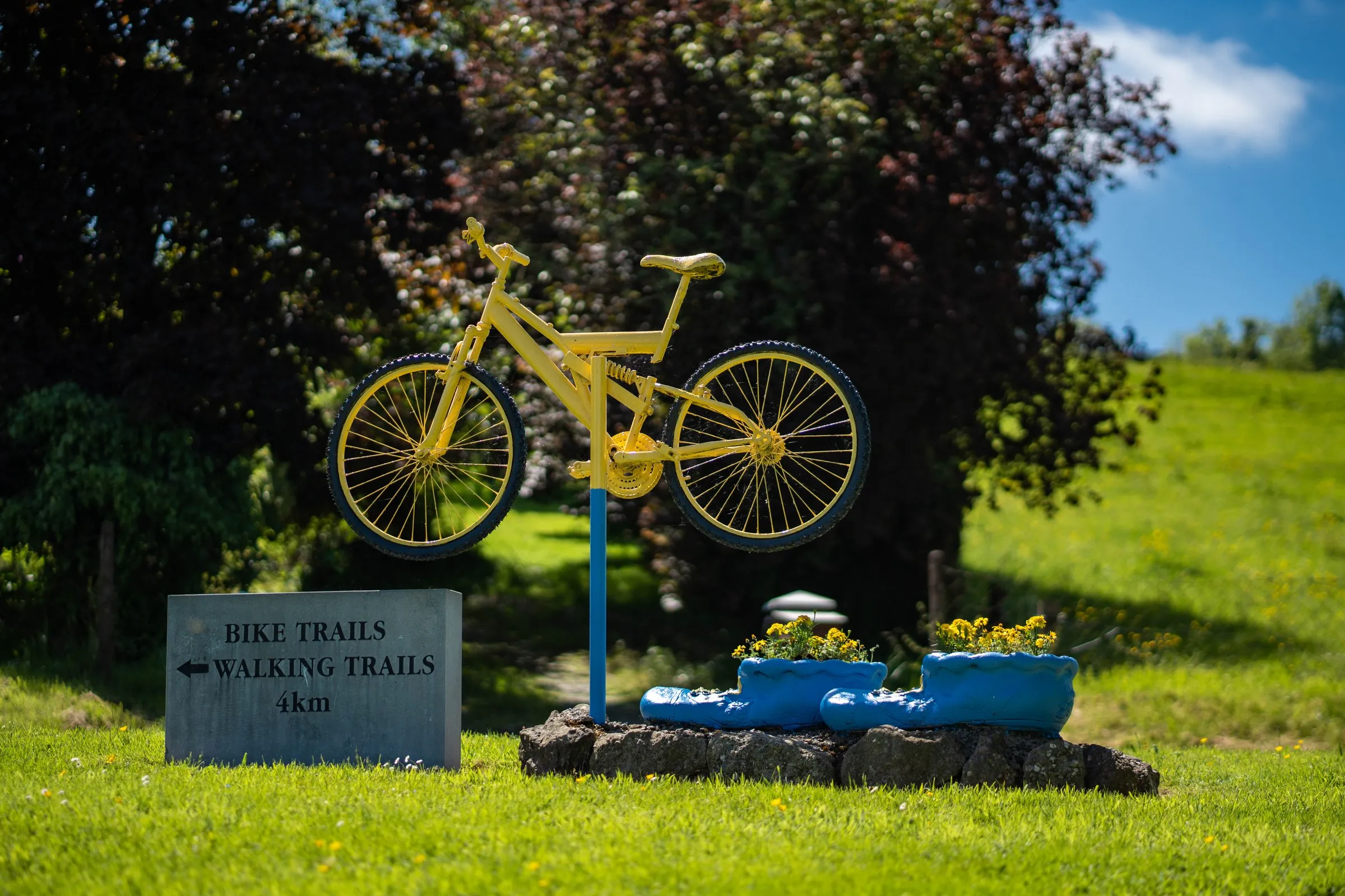 A yellow bicycle sculpture on a blue pole stands beside a sign for bike and walking trails.