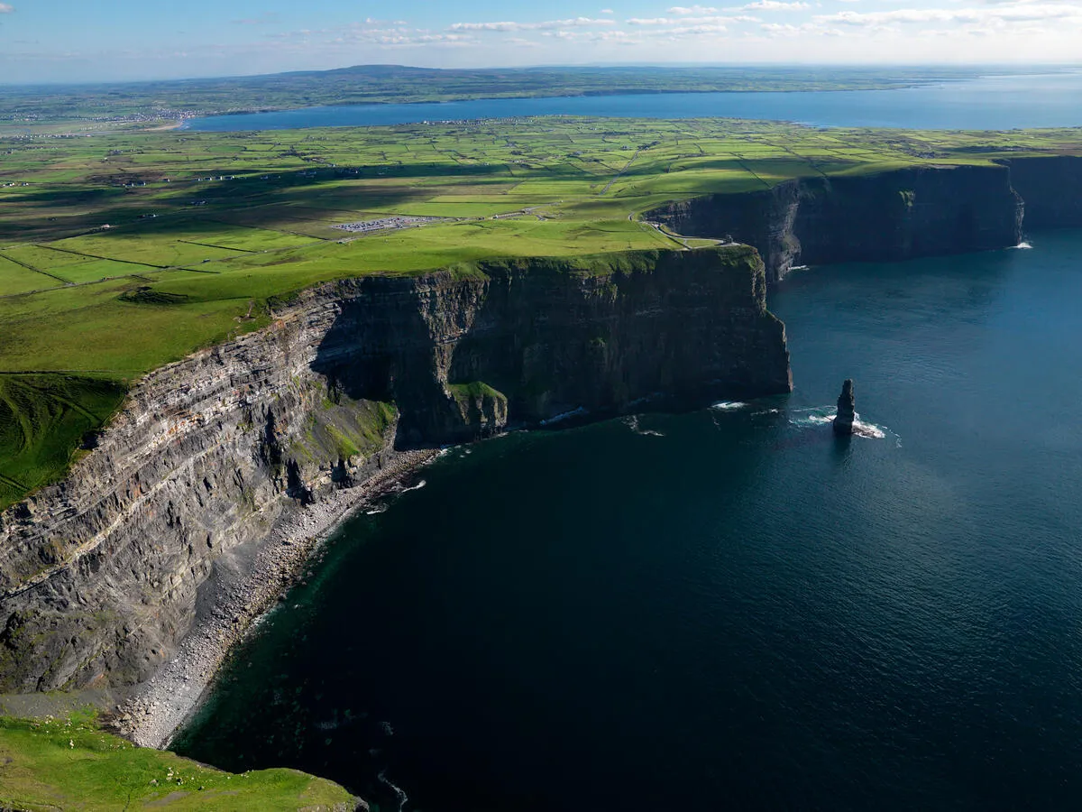 Aerial view of the Cliffs of Moher showing steep rock faces, green fields, and the sea.