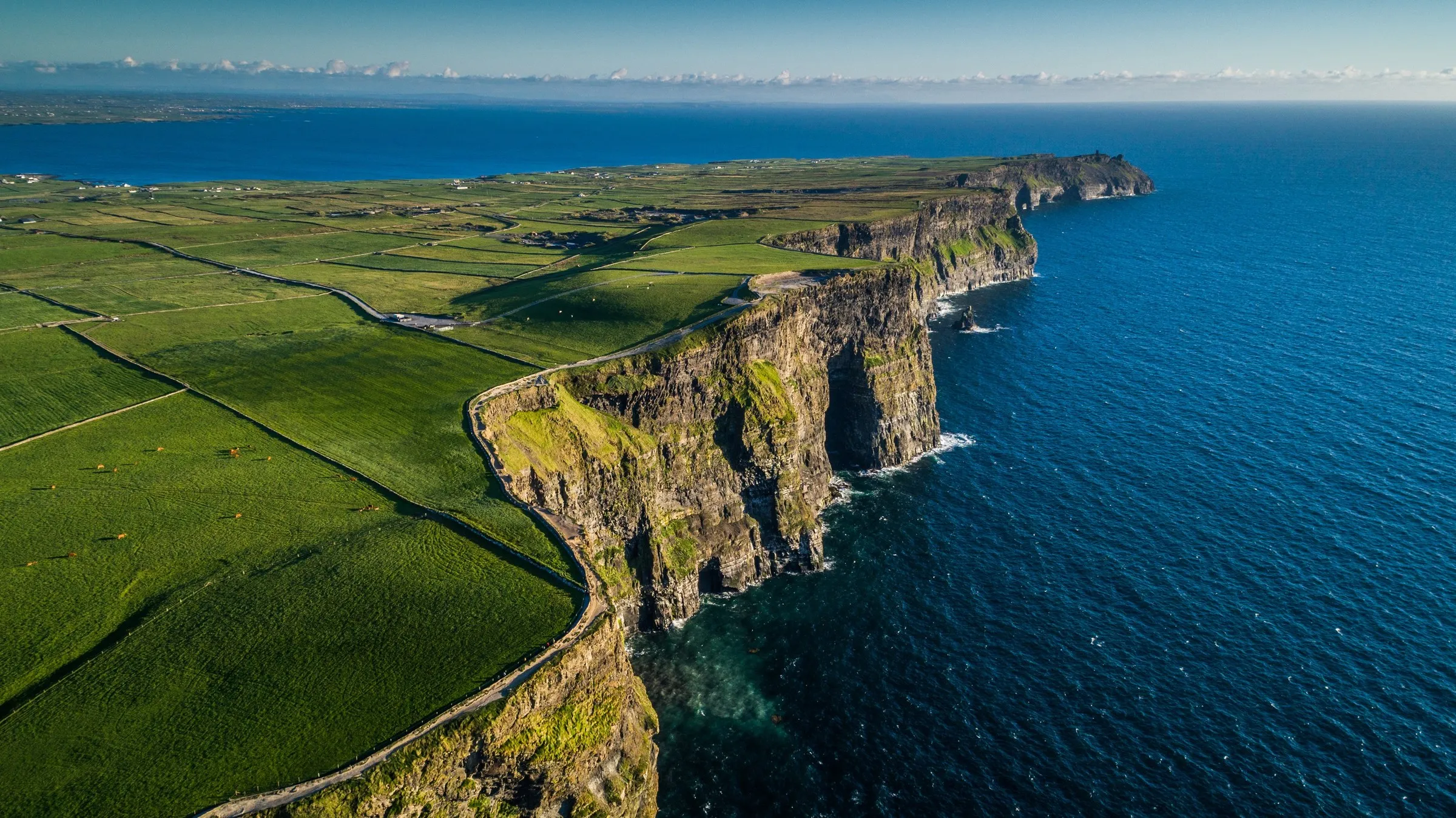 Aerial view of the Cliffs of Moher showing a winding road, green fields, and blue ocean.