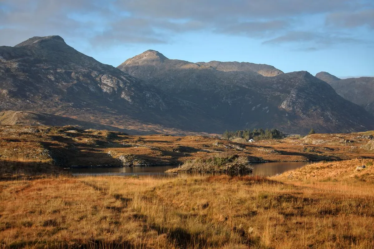 A landscape view of Inagh Valley showing golden grassy fields, a small pond, and large mountains in the background.