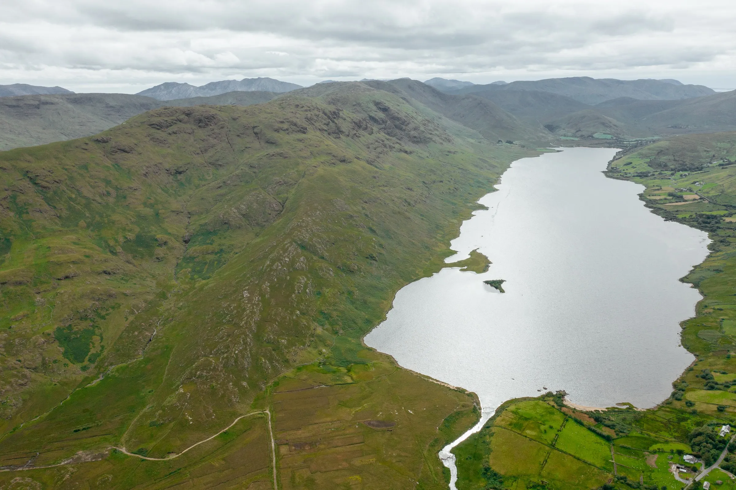 Aerial view of Lough Nafooey winding through green hills and mountains under a cloudy sky.